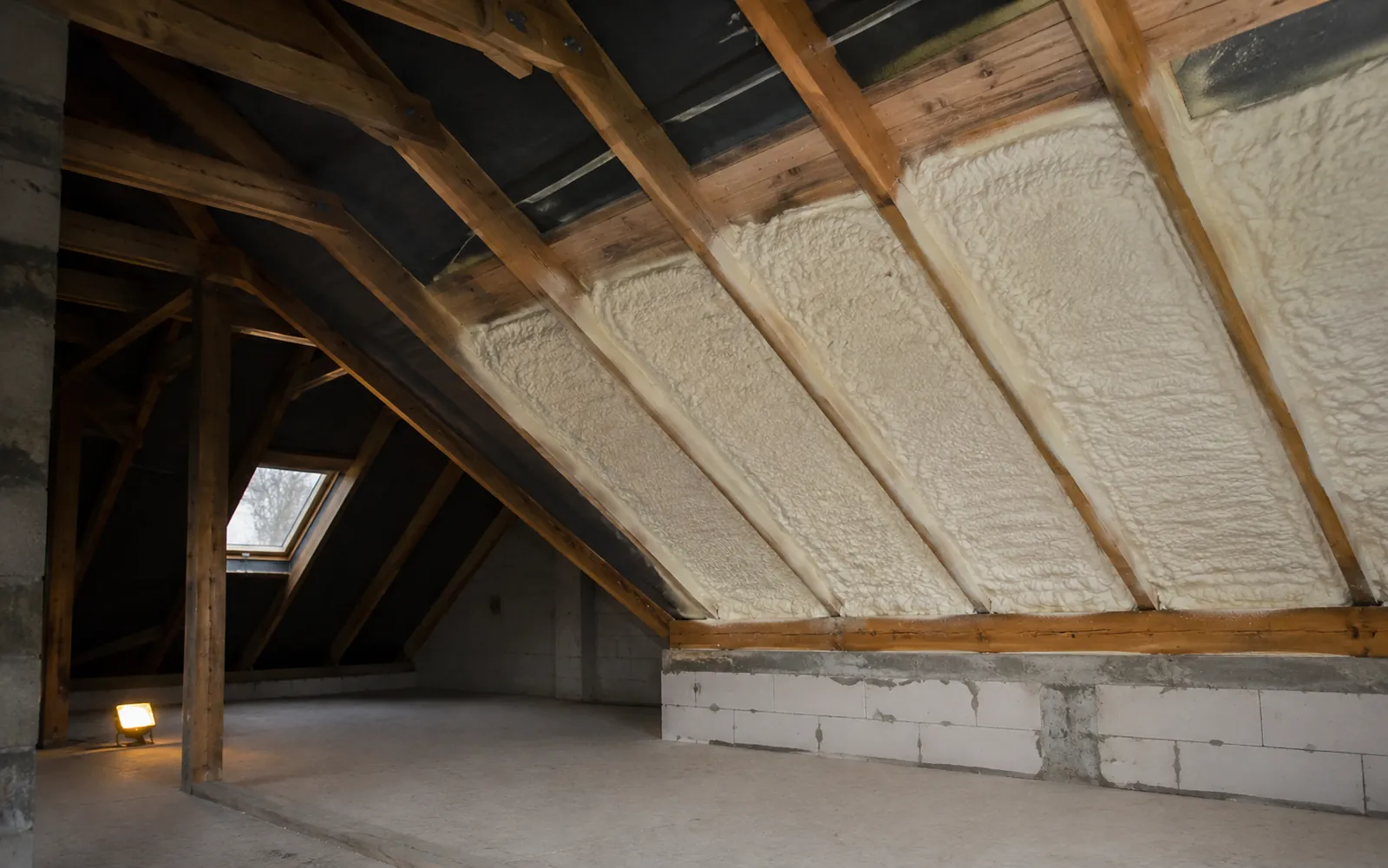 Wnętrze poddasza z widoczną drewnianą więźbą dachową i ciągłą warstwą jasnej piany PUR natryśniętej między krokwiami.